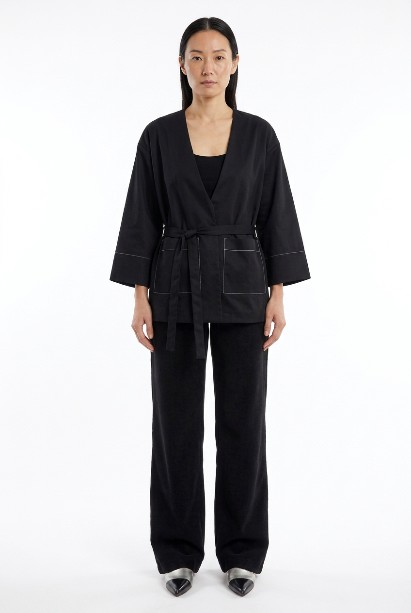Asiatisches Model mit schwarzer Bindegürtel-Jacke, Wide-Leg-Hose und schwarz-silbernen Schuhen