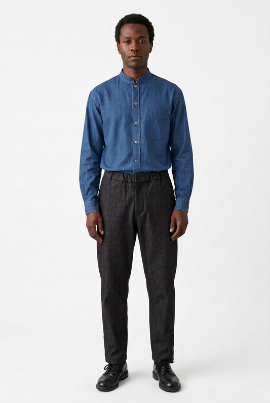 Männermodel mit Jeanshemd, dunkler Hose und schwarzen Schnürschuhen vor weißem Hintergrund