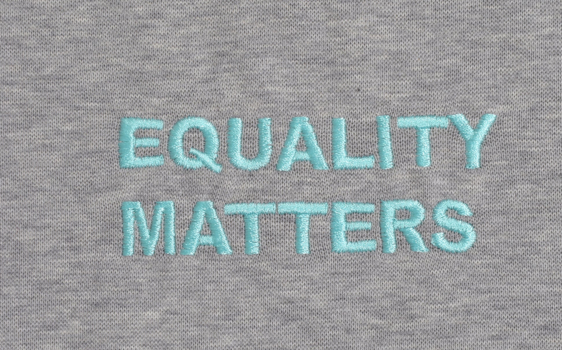 Stickerei "Equality Matters" in türkis blau auf grauem T-Shirt. Die Stickerei wird in Hamburg gefertigt. T-Shirt Made in Hamburg