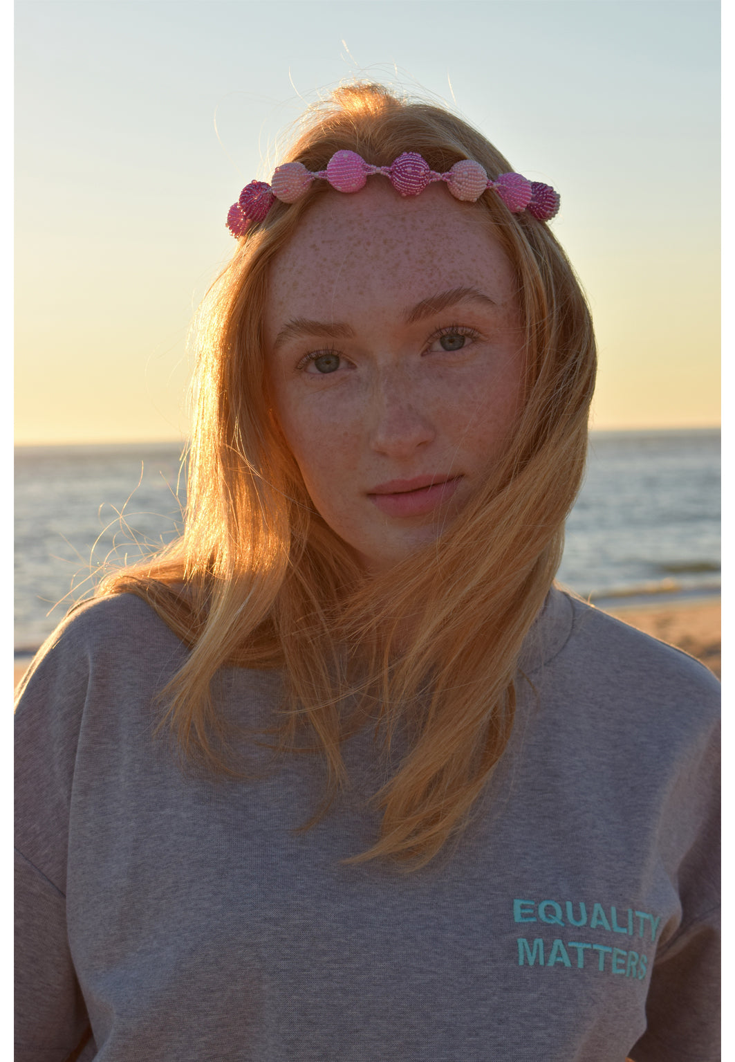 Junge Frau mit rötlichem Haar mit Kopfschmuck in grauem HEL T-Shirt mit Stickerei "Equality Matters" Rundhals! Made in Hamburg Sommerliches Bild am Strand von Sylt 